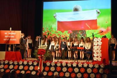 Uczniowie ZSP prowadzą uroczystą akademię na scenie. W tle flaga Polski.