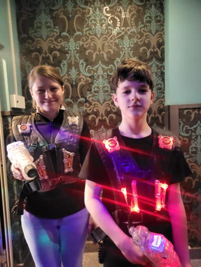 Uczeń wraz nauczycielką pozuje do zdjęcia ubrany w kamizelkę  i wyposażony w pistolet do rozgrywki Lasershot.