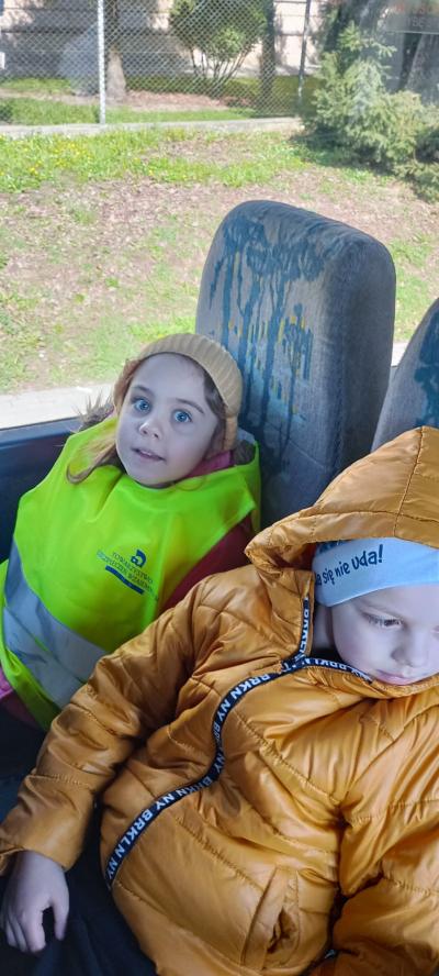 Chłopiec i dziewczynka w kamizelce odblaskowej w autobusie, patrza w stronę fotografującego.