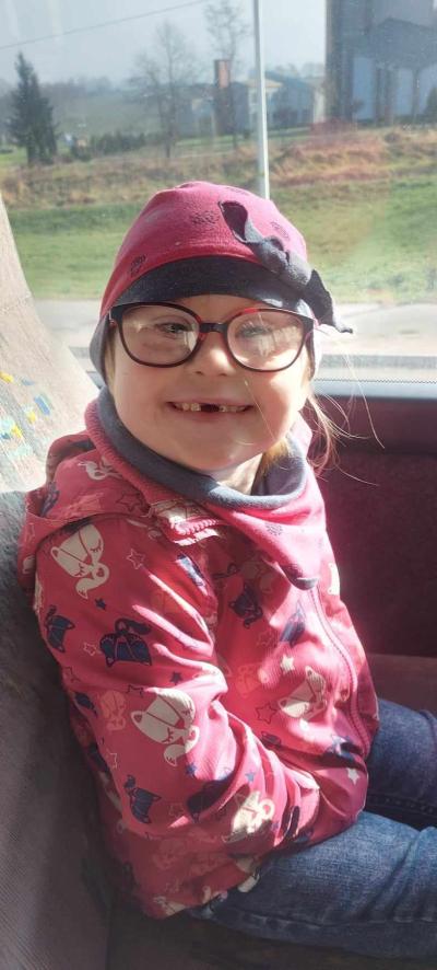 Dziewczynka w okularach siedzi w fotelu w autobusie i pozuje do zdjęcia, uśmiecha się.