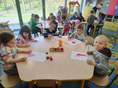 3 chłopców i 2 dziewczynki siedzą przy stoliku i malują farbami szablon skarpety. W tle inne dzieci pracujące przy stoliku.