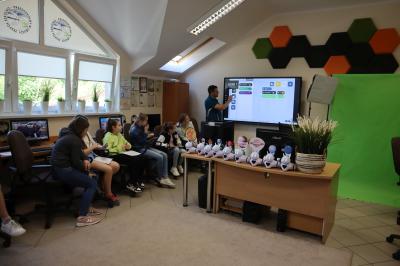 Nauczyciel tłumaczy uczniom na monitorze interaktywnym jakich bloków mają użyć aby zaprogramować robota Photona