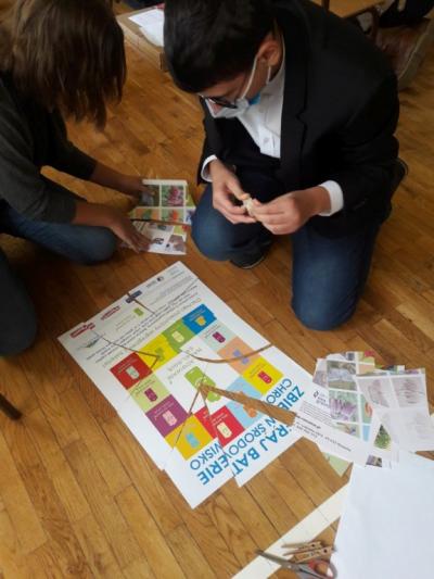 Uczniowie pracują w parach. Sklejają puzzle dotyczące sposobów ochrony środowiska. Na podłodze fragmenty plakatu. Uczniowie sklejają i tworzą plakat.