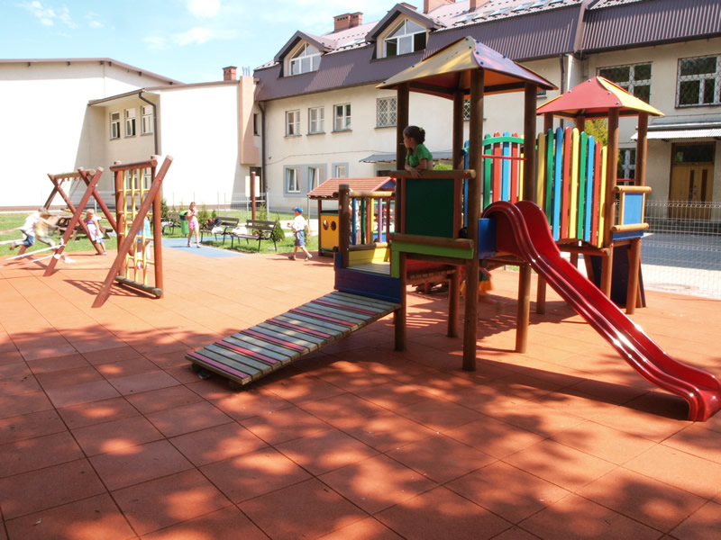 Plac zabaw przedszkola połozony za budynkiem szkoływraz z bawiącymi się dziećmi