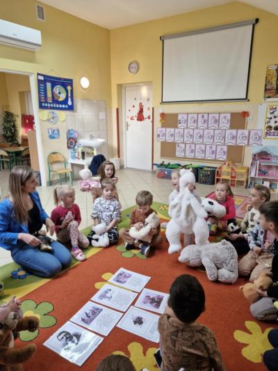 Pani siedzi razem z dziećmi na dywanie, przed nimi leżą kartki.jpg