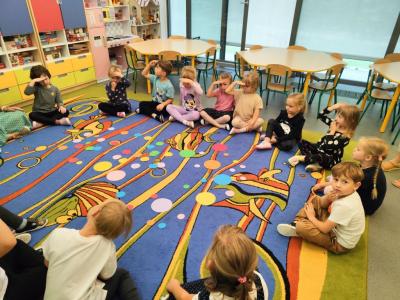 Dzieci siedzą na dywanie i szukają kropek na dywanie we wskazanym kolorze..jpg