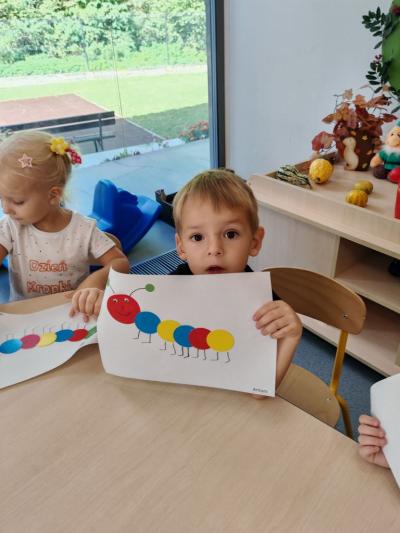 Chłpoczyk z grupy krasnali pokazuje swoją prace plastyczną na której widac stonogę z kółek..jpg
