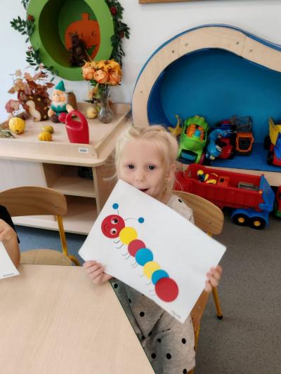 Dziewczynka z grupy krasnali pokazuje swoją prace plastyczną na której widać stonogę z kółek..jpg