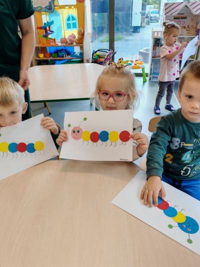 Dziewczynka z grupy krasnali pokazuje swoją prace plastyczną na której widac stonogę z kółek. (6).jpg