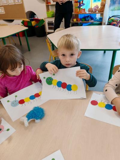 Dziewczynka z grupy krasnali pokazuje swoją prace plastyczną na której widac stonogę z kółek. (8).jpg
