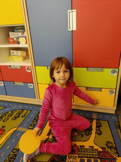 Dziewczynka z grupy krasnali trzyma w ręce koło w kolorze zóltym i placem wskazuje półkę w tym samym kolorze..jpg