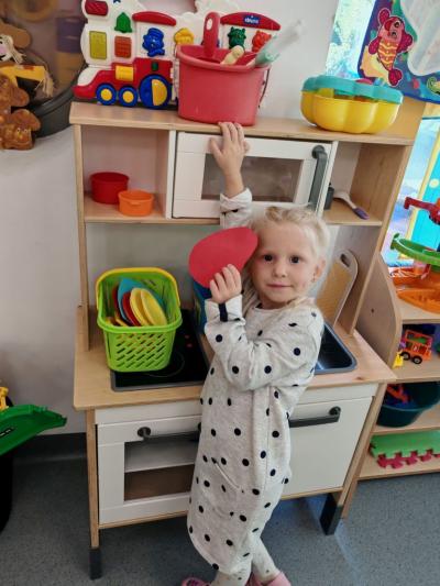 Dziewczynka z grupy krsanali stoi przy zabawkoej kuchence i wskazuje placem pojemnik..jpg