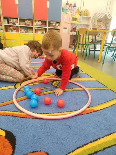 Dziewczynka i chłopiec segregują niebieskie i czerwone piłeczki w hulahop..jpg