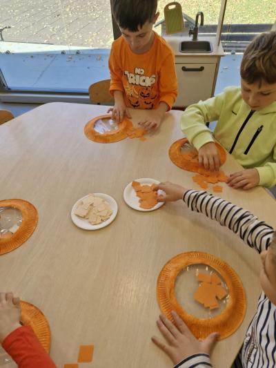 Dzieci siedzą przy stoliku i wykonują pracę plastyczną - Dynia.jpg