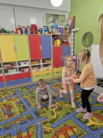 Dzieci stoją na dywanie i podają sobie dynie.jpg