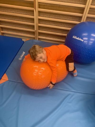 Chłopiec leży na pomarańczowej  dużej piłce w sali ćwiczeń..jpg