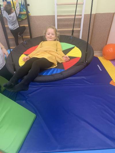 Dziewczynka leży na huśtawce typu bocianie gniazdo w sali ćwiczeń..jpg