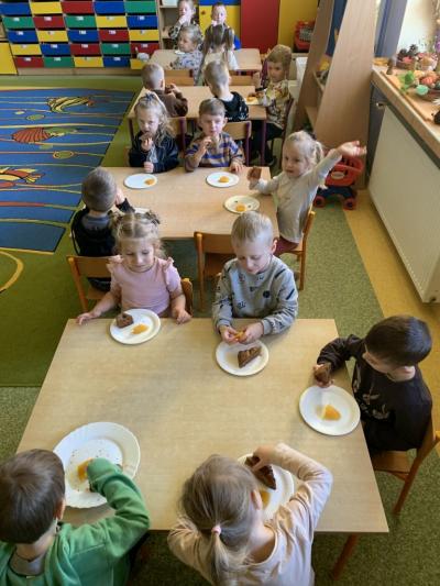 Dzieci siedzą przy stolikach i degustują się ciastem i musem położonym na papierowych talerzykach..jpg