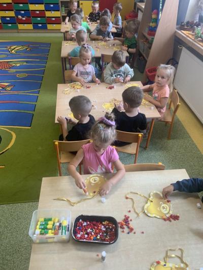 Dzieci siedzą przy stolikach i ozdabiają kolorowymi kuleczkami z bibuły sylwetę misia..jpg