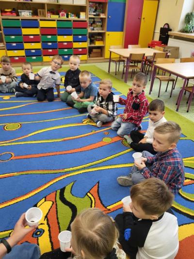 Dzieci siedzą w kręgu w sali przedszkolnej i trzymają w dłonich plastikowe kubeczki..JPG