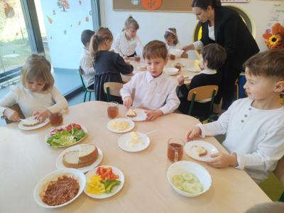 Dziewczynka i dwóch chłopców robią kanapki. W tle inne dzieci..jpg