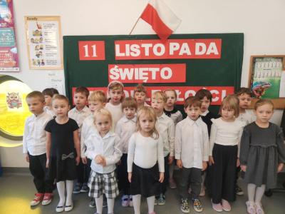 Dzieci z grupy Sówki śpiewają hymn. W tle tablica z  dekoracją..jpg