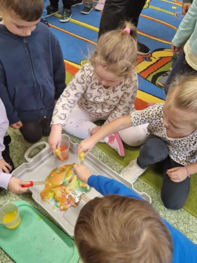 Kilkoro dzieci trzyma w dłoniach małe pipety. Upuszczając kolorowe krople barwią koronę drzewa zrobioną z wacików..JPG