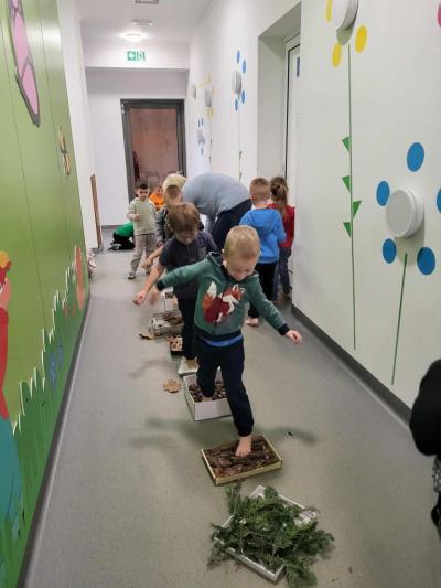 Rząd dzieci przechodzi boso po tackach z materiałem przyrodniczym ustawionych na korytarzu przedszkolnym..JPG