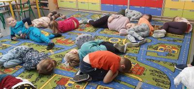 Dzieci z gr.Skrzaty leża na dywanie podczas zabawy do piosenki 
