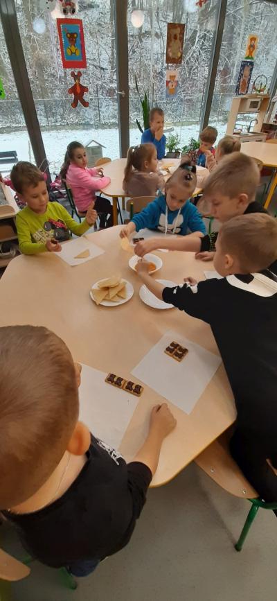 Dzieci z grupy Skrzaty siedzą przy stolikach i degustują miód oraz misiowe ciasteczka.
