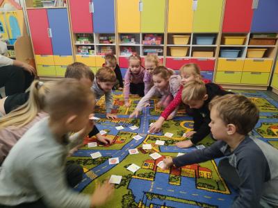 Dzieci siedzą na dywanie i wybierają kartoniki z rysunkami owoców.
