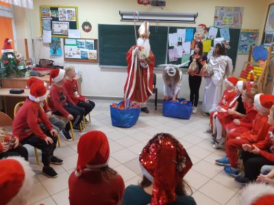 Święty Mikołaj wręcza prezenty dzieciom w klasie. Pomagają mu aniołki i diabełek.