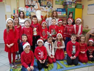 Dzieci wraz Świętym Mikołajem pazuja do zdjęcia. Wszyscy ubrani w czerwone stroje.