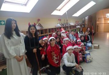 Zdjęcie klasy 5a zrobione na górnym korytarzu. Uczniowie ubrani w czerwone elementy garderoby. Pomiędzy nimi siedzi Św. Mikołaj, a obok stoi dziewczynka w stroju aniołka i ubrany na czarno diabełek.
