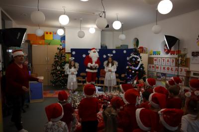 Dzieci przychodzą na spotkanie ze Świętym Mikołajem. Mikołaj w asyście aniołków przemawia do dzieci. W tle piękna dekoracja świąteczna.