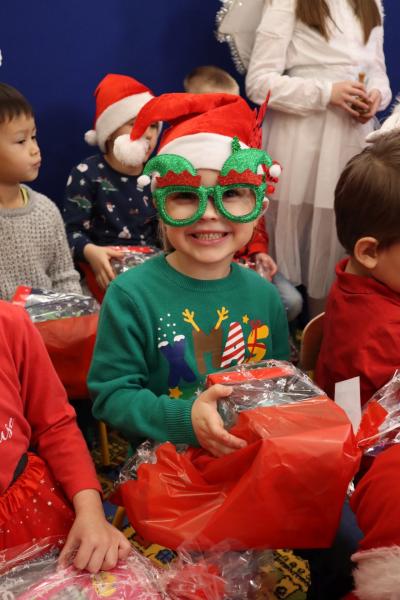 Święty Mikołaj podczas spotkania z przedszkolakami. Dzieci ubrane w mikołajkowe stroje śpiewają piosenki mikołajowi.
