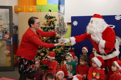 Święty Mikołaj podczas spotkania z przedszkolakami przybija piątki dzieciom lub wręcza prezenty.