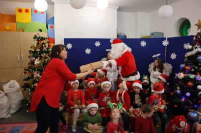 Święty Mikołaj podczas spotkania z przedszkolakami przybija piątki dzieciom lub wręcza prezenty.