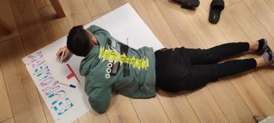 Chłopiec leżąc na podłodze maluje plakat z hasłem obozu EuroWeek.