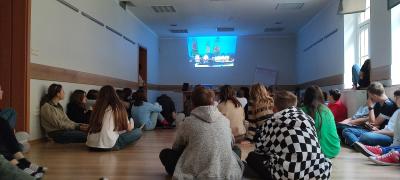Uczestnicy obozu językowego siedzą na podłodze i oglądają film wyświetlony na ścianie.