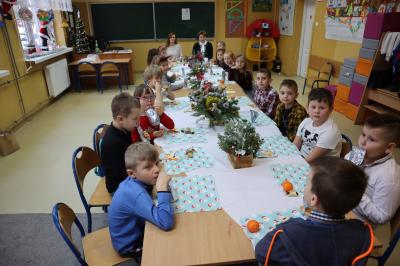 Uczniowie siedzą przy wigilinych stołach. Na stole stoiki, potrawy, słodkości.