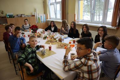 Uczniowie siedzą przy wigilinych stołach. Na stole stoiki, potrawy, słodkości.