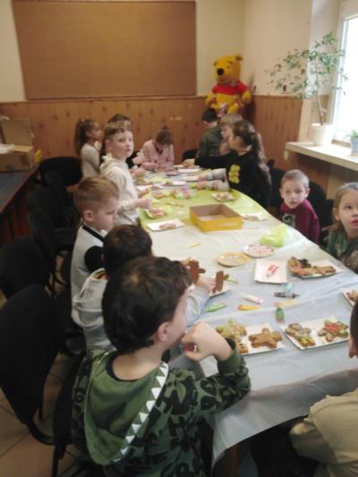 Uczniowie siedzą przy stolikach i dekorują piernikowe misie.