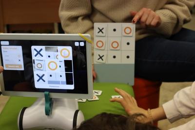 Uczniowie grają w grę kółko i krzyżyk ze sztuczną inteligencją obsługiwaną przez robota photon.