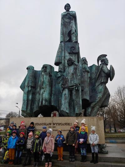 Dzieci stoją pod pomnikiem Stanisława Wyspiańskiego