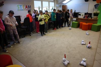 Uczniowie klasy 3b podzieleni na 3 drużyny sterują robotami Photon. Roboty poruszają się po dywanie a dzieci sterują nimi za pomocą tabletów.