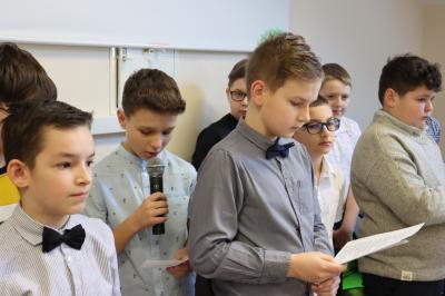Odświętnie ubrani chłopcy z klasy Vb recytują wiersze oraz przekazują życzenia z okazji dnia kobiet.