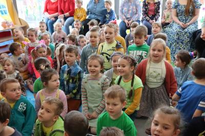 Całe zdjęcie wypełniają przedszkolaki siedzące na dywanie i śpiewajace piosenkę.