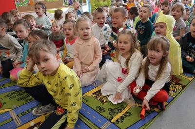 Całe zdjęcie wypełniają przedszkolaki siedzące na dywanie i śpiewajace piosenkę.