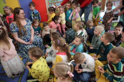 Nauczycielka śpiewa z dziećmi piosenkę, wszyscy siedzą na dywanie.